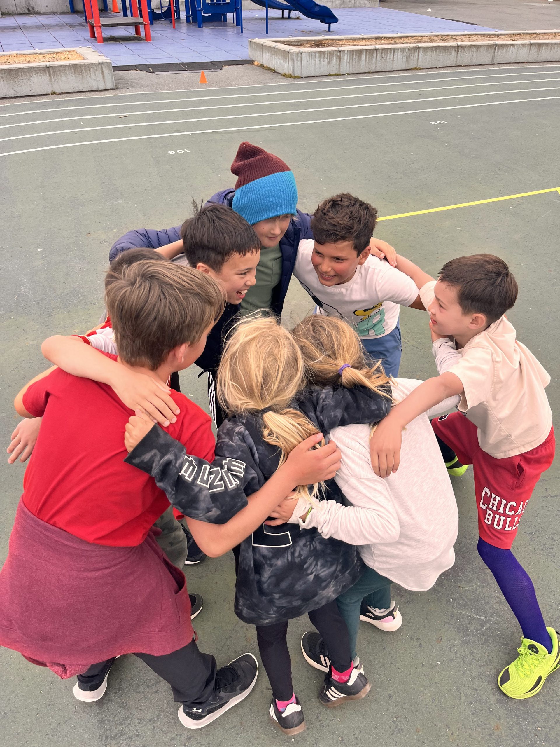 Children gathering together in a huddle on an outdoor court.