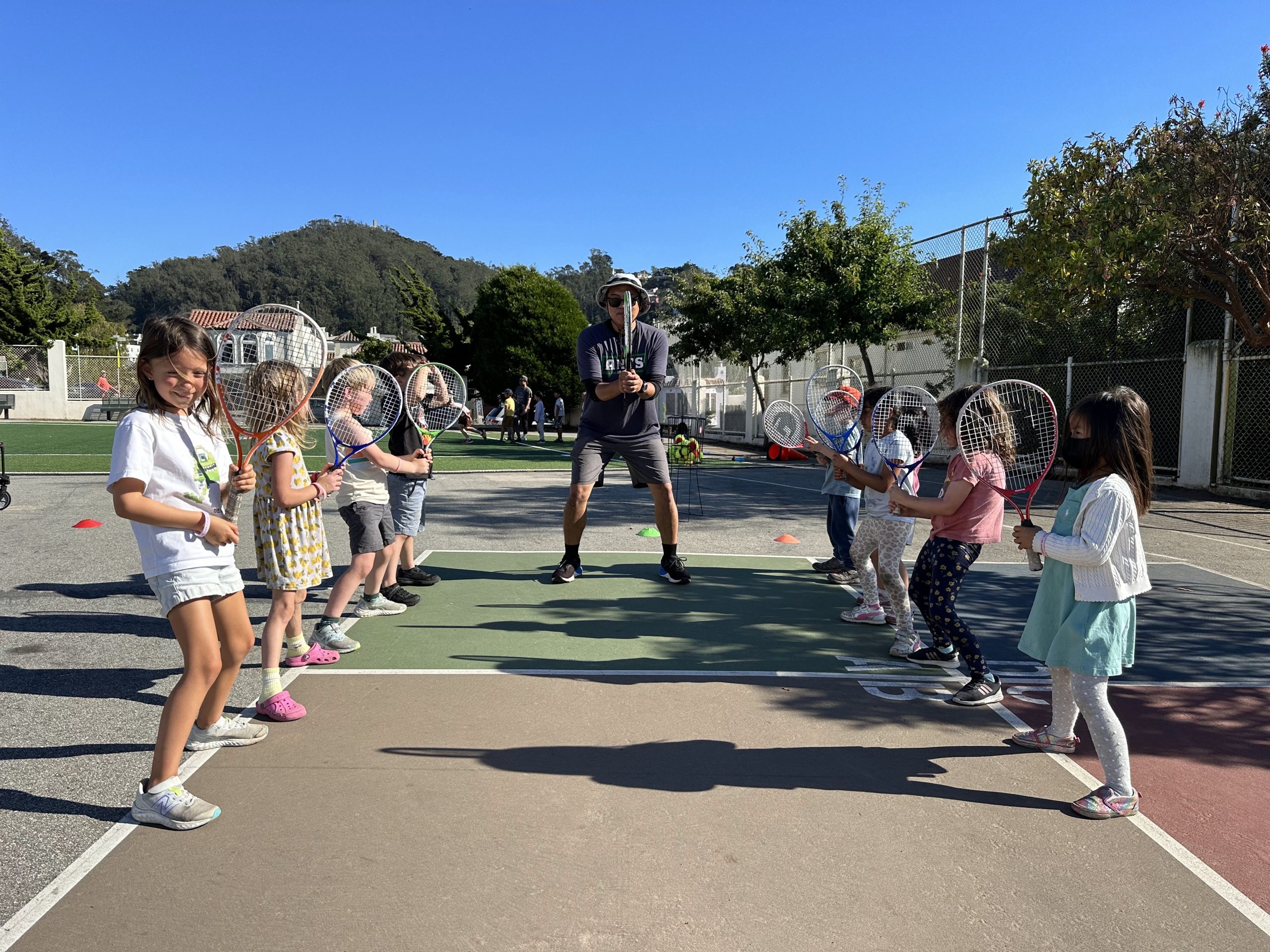 Children holding tennis rackets in two lines with a coach between them.