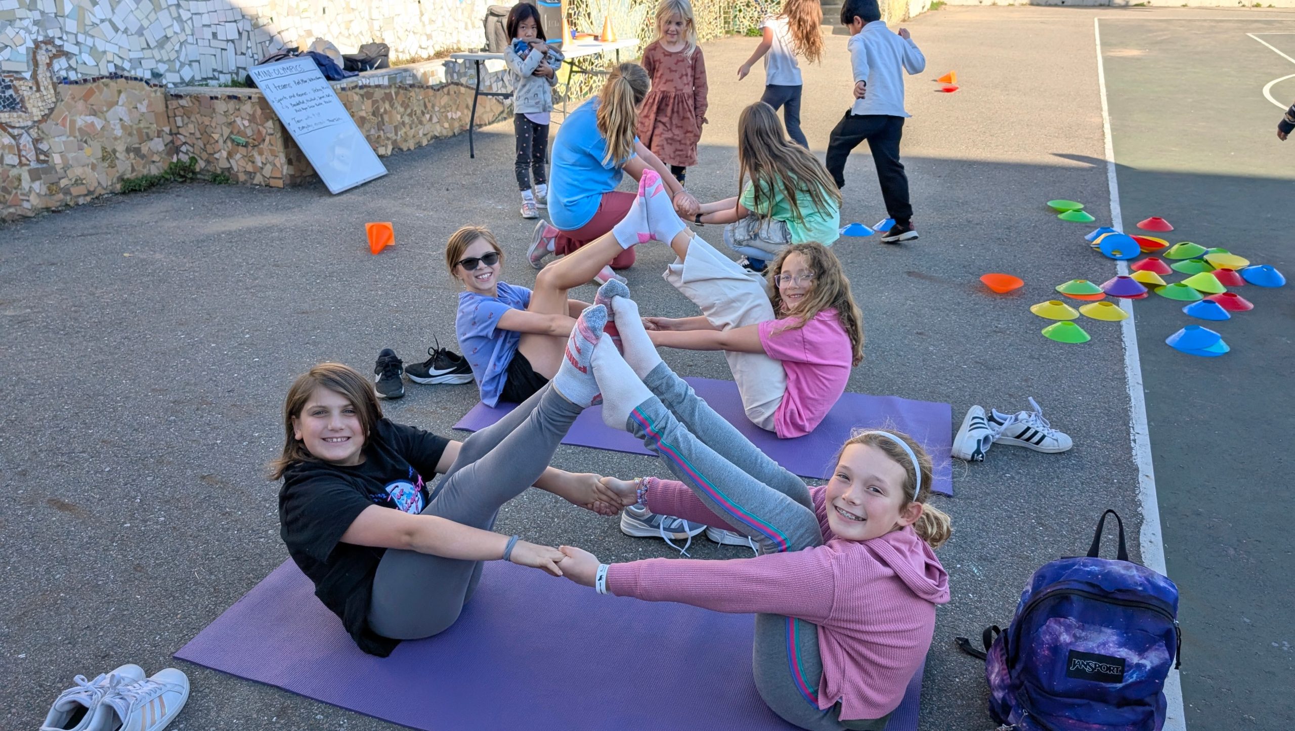 Children sitting together and stretching on mats outdoors.