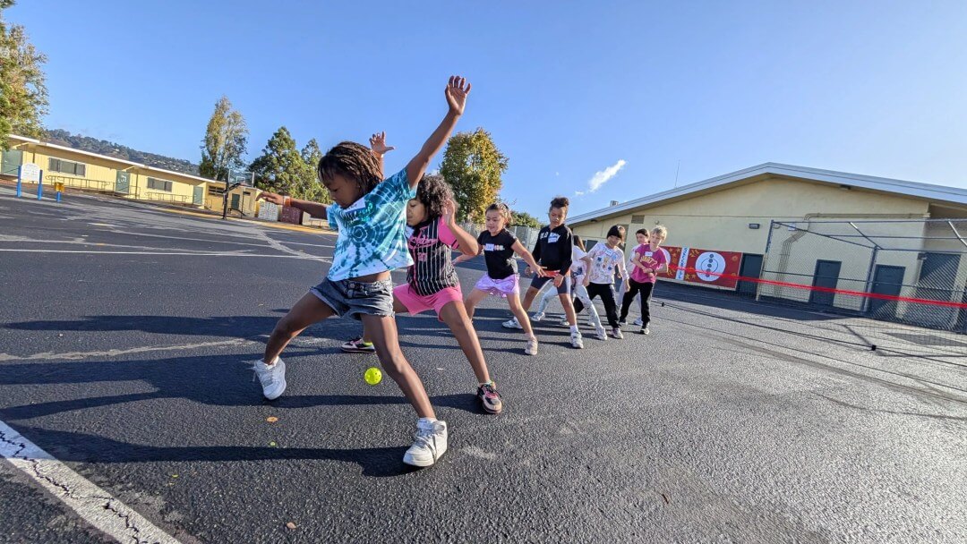 Children practicing tennis strokes on a school playground.