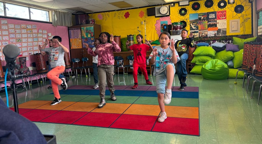 Children practicing martial arts kicks in a classroom.