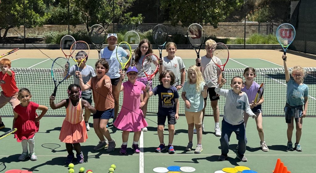 Children and coaches posing with tennis rackets on an outdoor court.