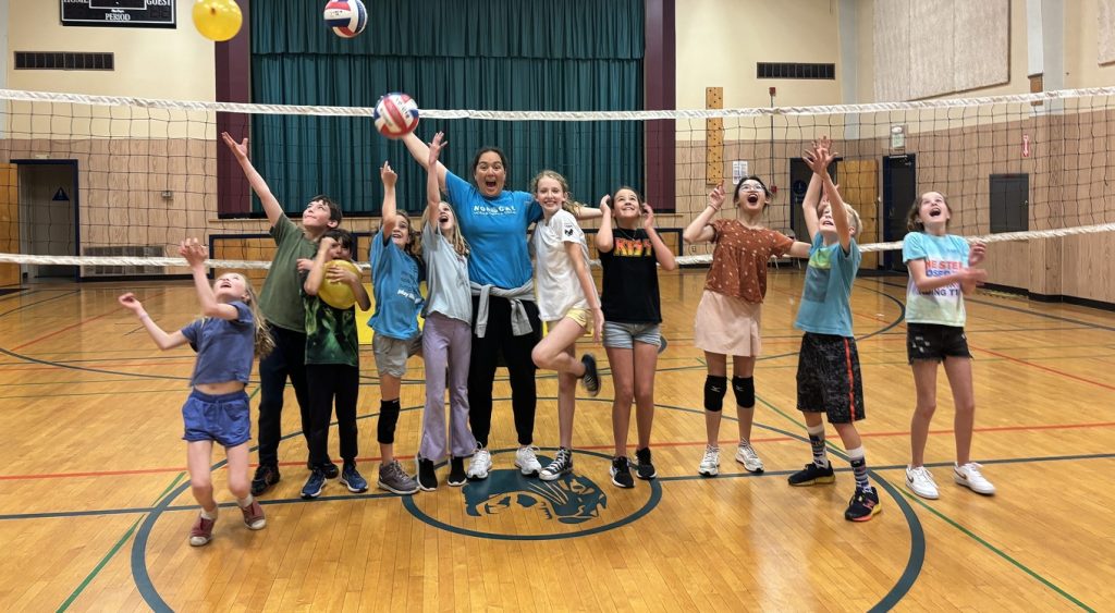 Children tossing volleyballs in an indoor gym.
