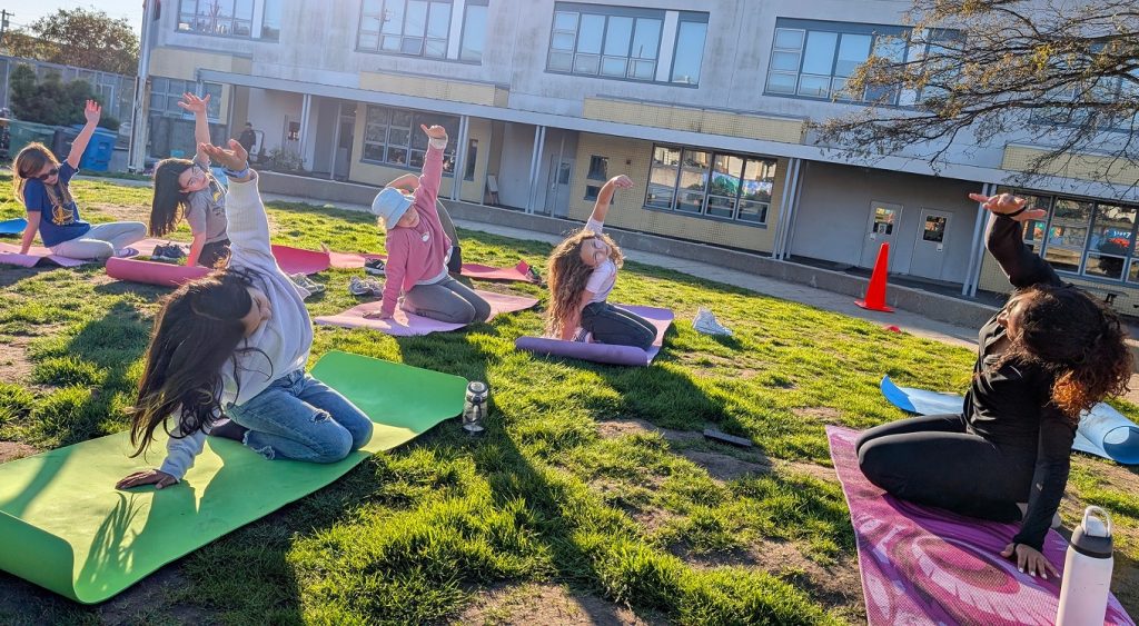 Children stretching on colorful yoga mats on the grass.