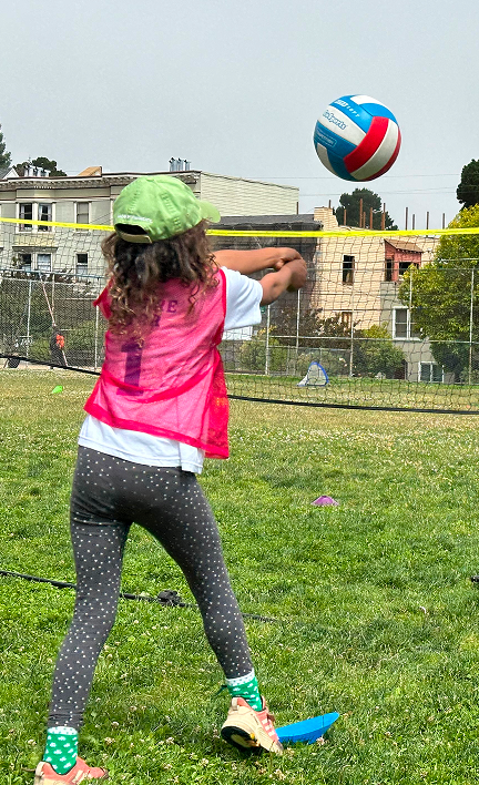 A child preparing to hit a volleyball over an outdoor net.