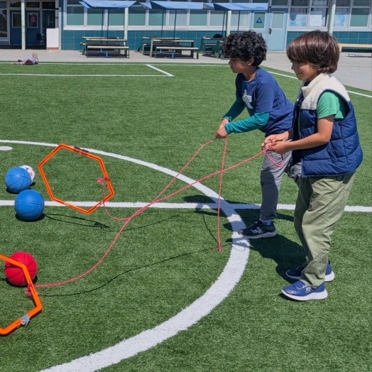 Children holding hoops and balls during an outdoor activity.