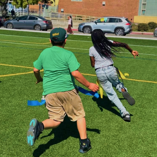 Children running across a grass field during a game.