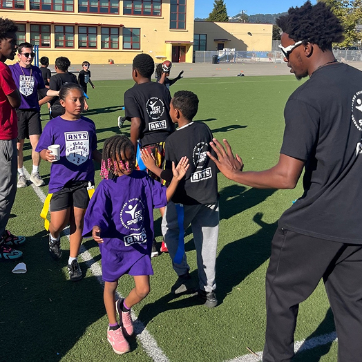 An ANTS coach giving high-fives to children on a field.