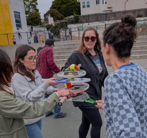 Adults balancing stacked tennis rackets during an outdoor activity.