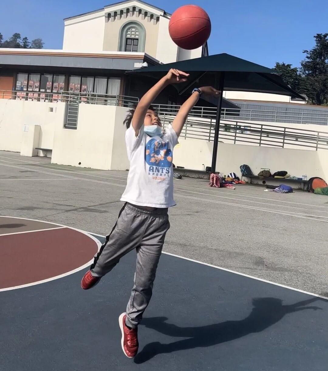 A child raising a basketball to take a shot on an outdoor court.