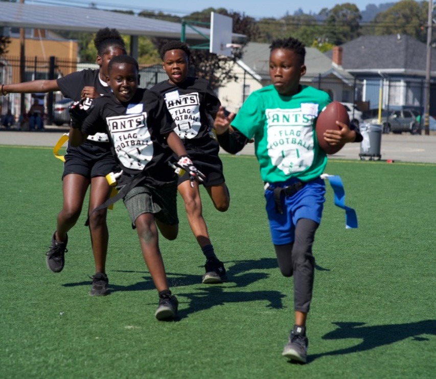 A child running with a football as other children follow on a field.