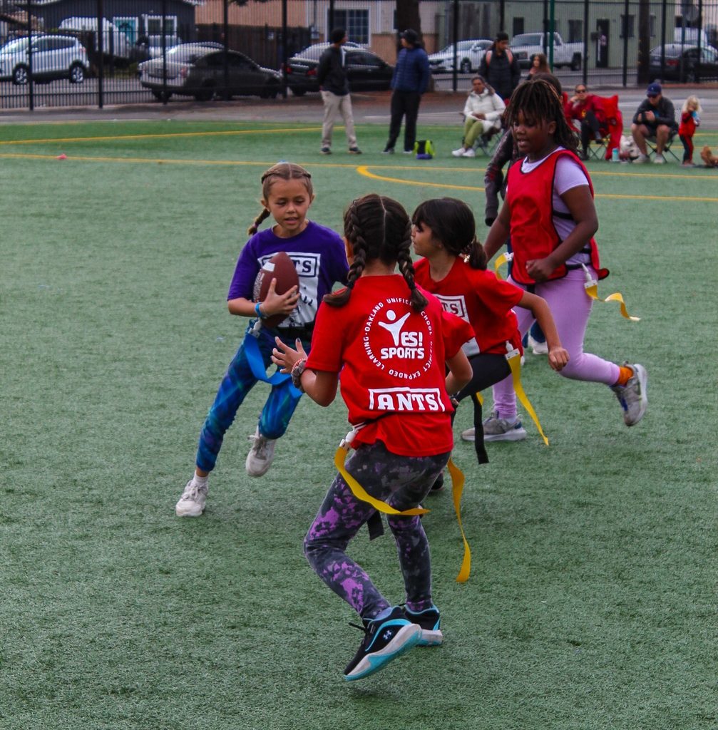 Children in red shirts playing flag football on a field.