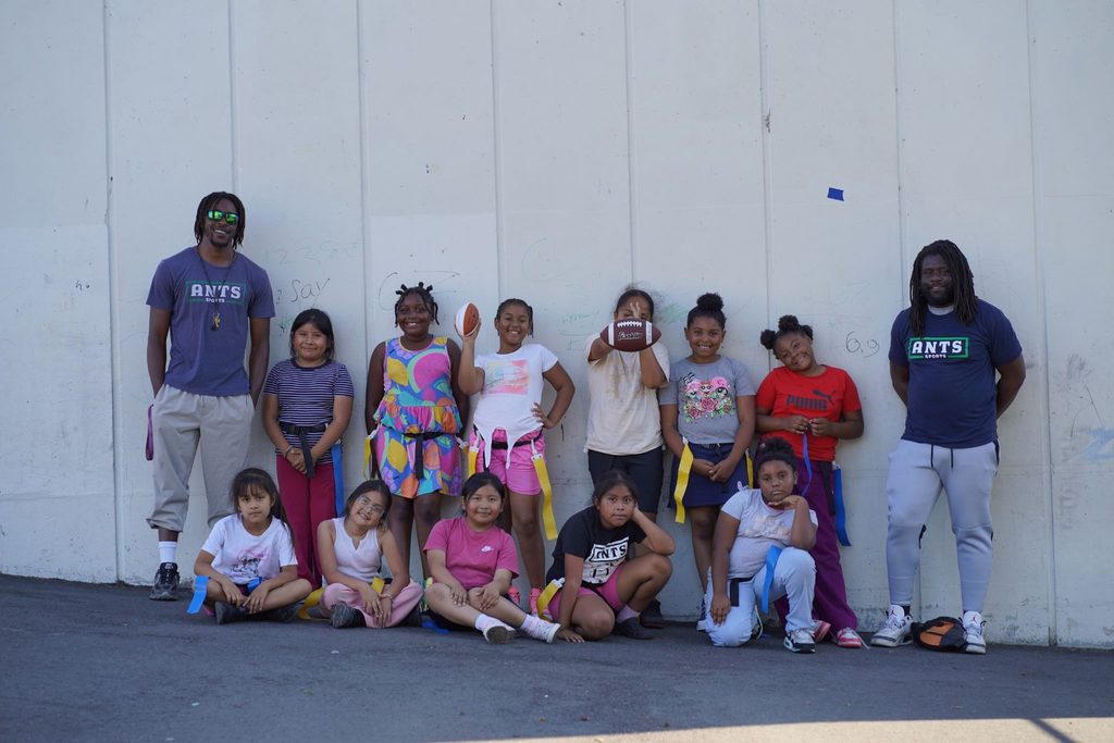 Children and ANTS coaches posing together in front of a wall.