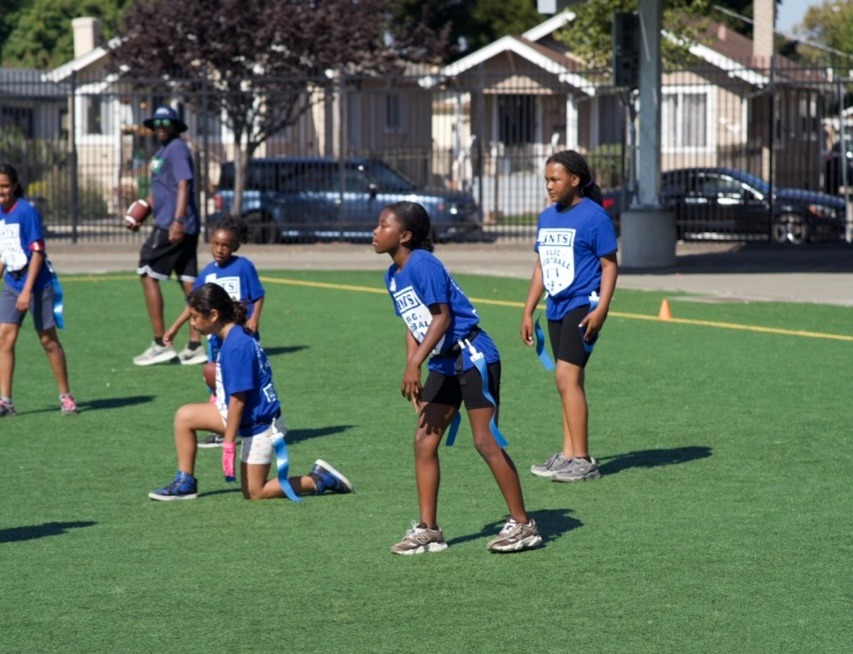 Children in blue shirts getting ready to play flag football on a field.