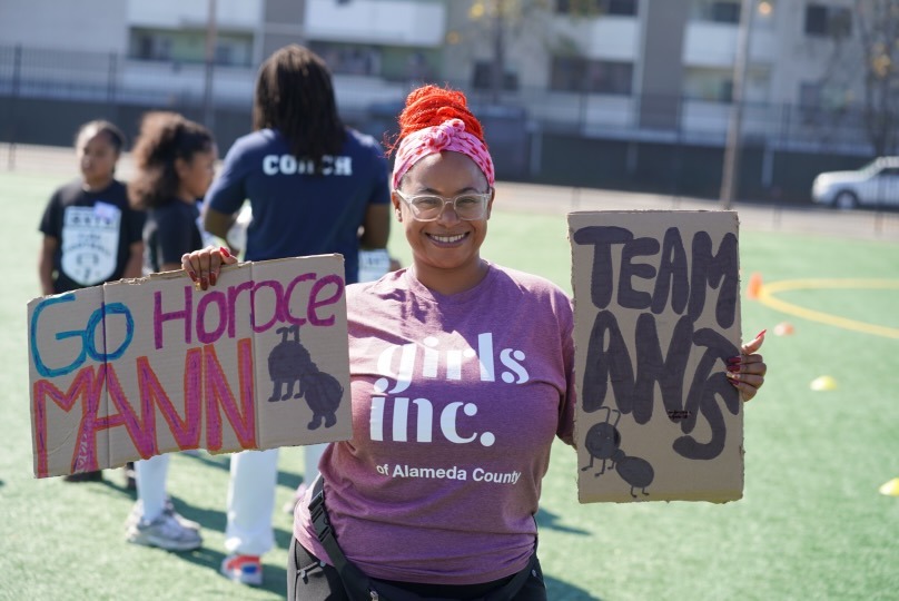 An ANTS coach holding handmade team support signs at a flag football event.