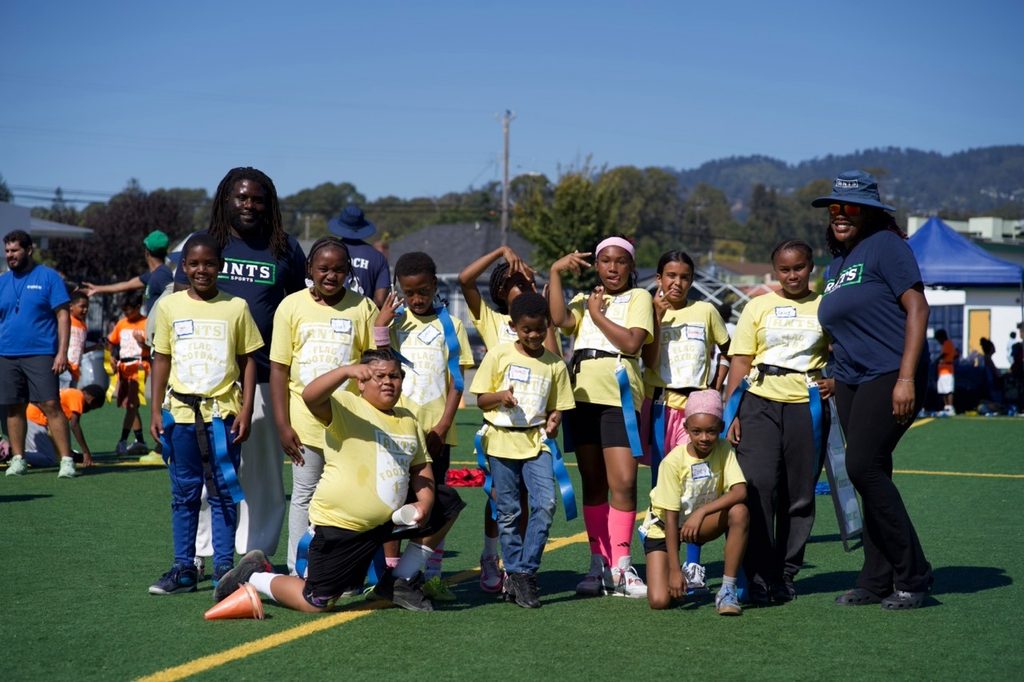 Children in yellow shirts and ANTS coaches posing together on a field.